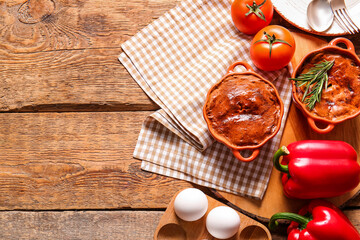 Board with delicious meat pies in baking forms and vegetables on wooden table