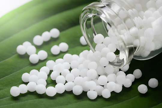 Homeopathic pills scattered from a bottle on a green leaf, close up