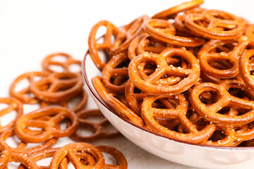 Bowl of tasty salted pretzels on light background, closeup