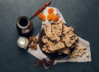 Composition with biscotti cookies, nuts, dried apricots, chocolate and coffee in cezve on black background