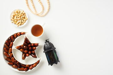 Ramadan Kareem greeting card. Crescent and star plate with dried dates, arabic lantern, cup of tea, nuts, rosary breads on white background