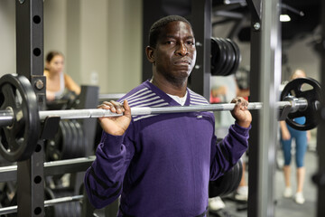 Fototapeta premium African-american man training with barbell using squat rack in gym