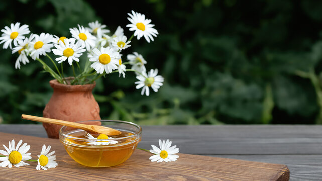 Chamomile syrup in a small bowl and in a jar in the patio on a wooden table
