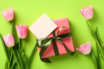Flat lay composition with tulips and gift box with empty greeting card on green background. Happy Mother Day concept.
