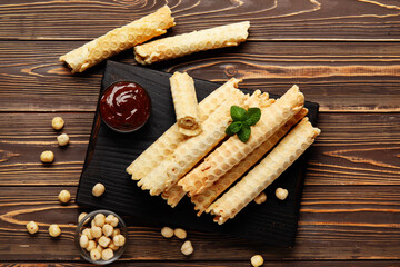 Board with delicious wafer rolls, boiled condensed milk and hazelnuts on brown wooden background