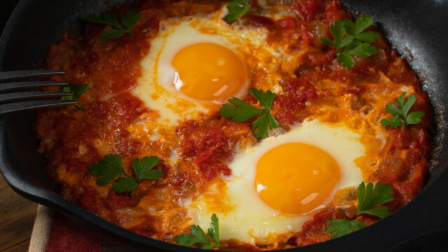 Two egg shakshuka in tomato sauce with fresh tomatoes, spices and herbs. Close-up scrambled eggs