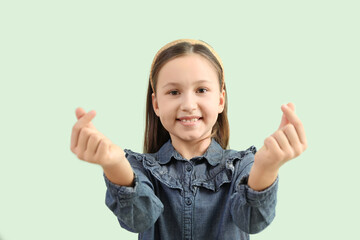 Cute little girl making heart with her fingers on green background, closeup