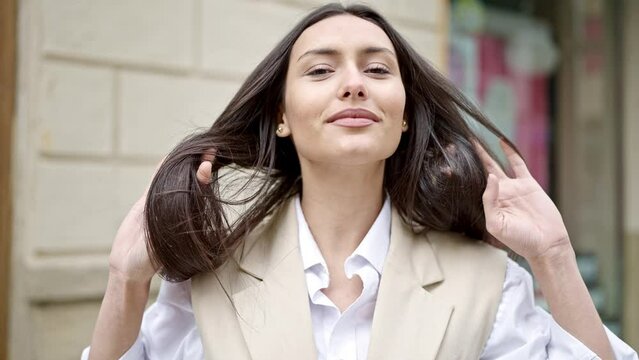 Young beautiful hispanic woman smiling confident combing hair with hands at street
