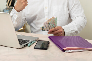 Horizontal view of Hispanic professional executive making a balance and counting money front their laptop in home office thinking while see the laptop