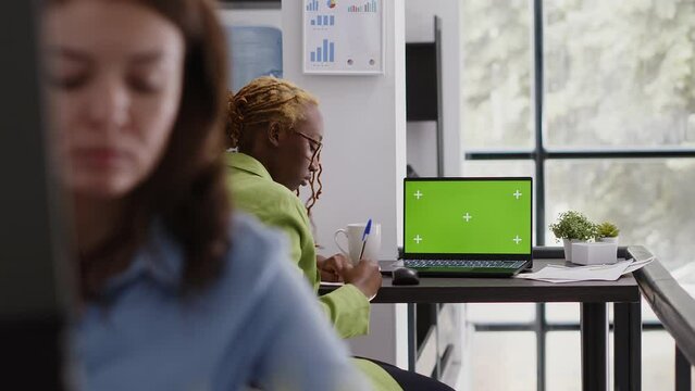 Executive assistant analyzing green screen display on pc, using laptop with chroma key copyspace display. Office employee looking at isolated mockup screen in business coworking space.
