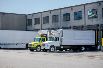 Affordable middle duty rigs semi trucks with refrigerated box trailers loading cargo standing in warehouse dock