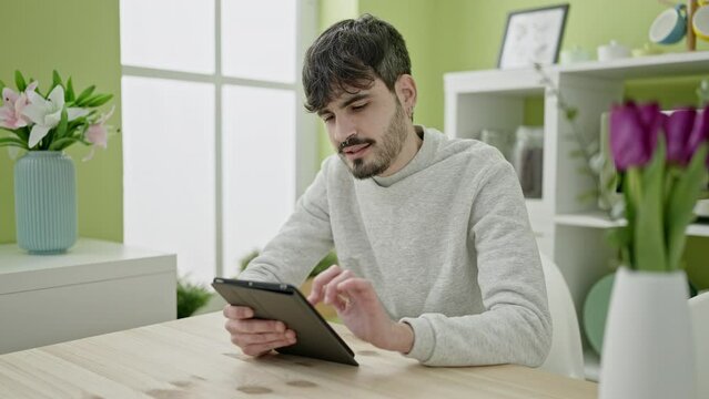 Young hispanic man using touchpad sitting on the table at dinning room