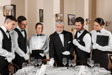 Senior man wearing formal suit teaching trainees in restaurant. Professional butler courses - obrazy, fototapety, plakaty
