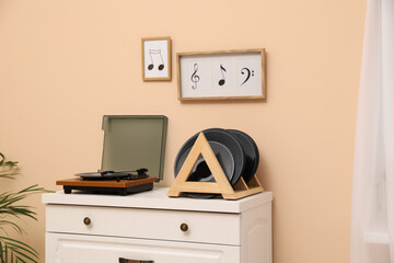 Vinyl records and player on white wooden drawer dresser near beige wall