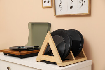 Vinyl records and player on white wooden drawer dresser near beige wall