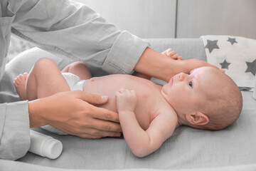 Mother taking care of her baby on changing table indoors, closeup