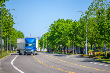Commercial freight blue big rig semi truck with dry van semi trailer turning on the city street at industrial area