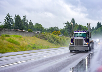 Fototapeta na wymiar Day cab classic big rig American semi truck with empty flat bed semi trailer driving on the wet slippery highway road at raining weather
