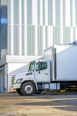 Middle duty day cab rig semi truck with box trailer for local business deliveries and moving standing on the city street parking lot with multi storey apartment building