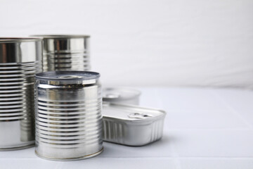 Many closed tin cans on white tiled table, closeup. Space for text