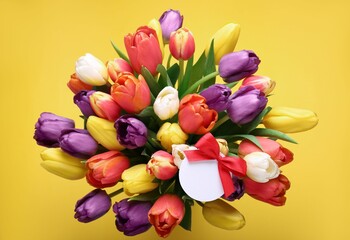 Bouquet of beautiful colorful tulips with blank card on yellow background, top view. Birthday celebration