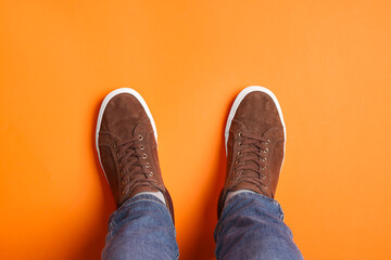Man in stylish sneakers standing on orange background, top view