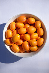 White bowl filled with small kumquats, in the sun