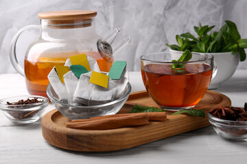Tea bags, cup of hot drink and ingredients on white wooden table