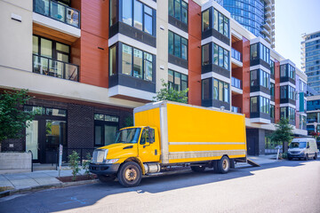 Yellow middle duty rig semi truck with box trailer and cargo mini van make a delivery to urban city apartment residential multi storey buildings