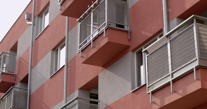 Facade of a house with balconies. Window openings with white frames. Rays of light, shadows design. Place of residence of people in the city. Metal pipe collecting rainwater.