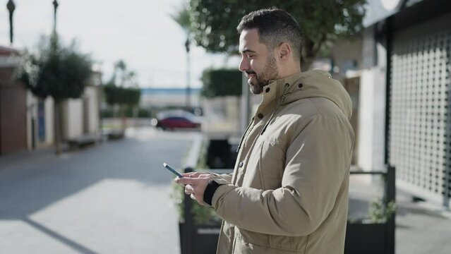 Young hispanic man smiling confident using smartphone at street
