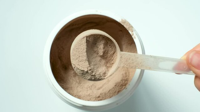 Female hand takes out protein powder in scoop from jar on white background top view.