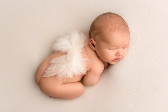 Top view of a newborn baby sleeping naked with angel wings on a white felt background. Beautiful portrait of a little newborn 7 days, one week old. Little newborn angel.