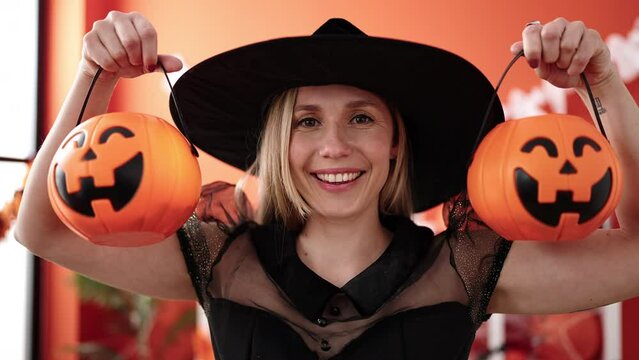 Young blonde woman having halloween party holding pumpkin baskets at home
