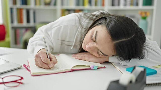 Young beautiful hispanic woman student writing notes tired at university classroom