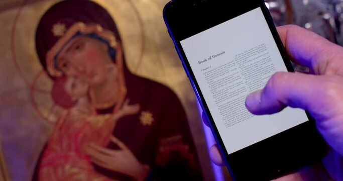 Close-up of the phone on the screen with the text of the Bible, on the background of the icon of the Madonna and Child. Reading religious texts before prayer.