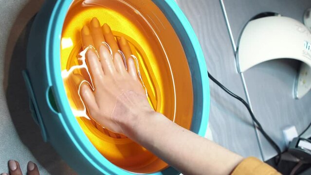 Manicure treatment with one hand having flannel glove and other being soaked with paraffin wax. Hand paraffin therapy in spa salon. Skin care. Cosmetology and skincare equipment. Wax bathtub care. 