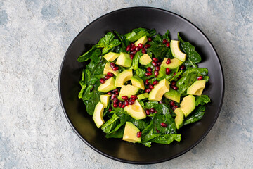 Avocado salad with spinach and pomegranate in a black plate on black background.