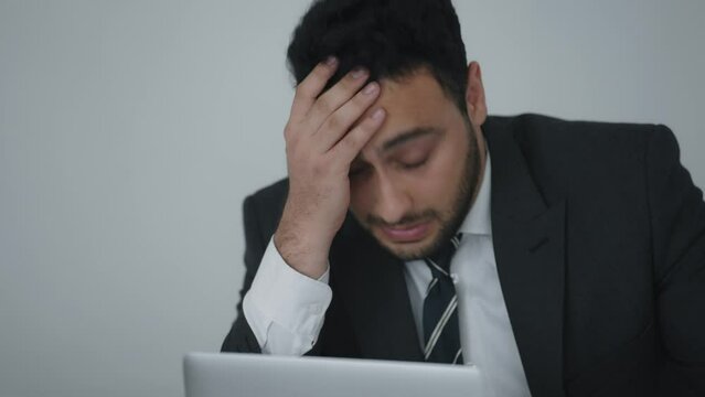 Indian businessman in a suit using labtop and being worried and irritated after receiving news about work at office
