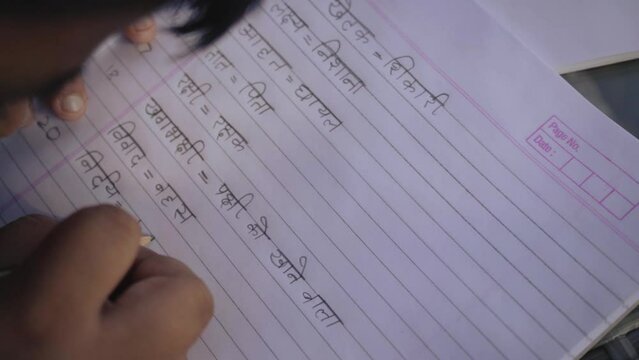 A kid studying and writing Hindi in a notebook.