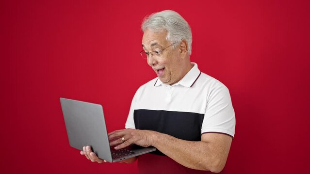 Middle age man with grey hair standing using laptop doing thumbs up over isolated red background