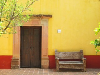 old mexican door with a yellow wall and wooden bench