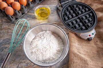 Baking ingredients with eggs, flour , oil  and light blue whisk. Home baking waffle concept.