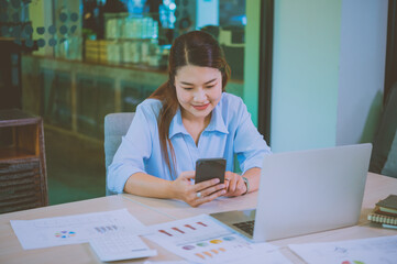 Fototapeta premium Business asian woman sitting at her desk with laptop using mobile phone during checking an email or social media on internet.