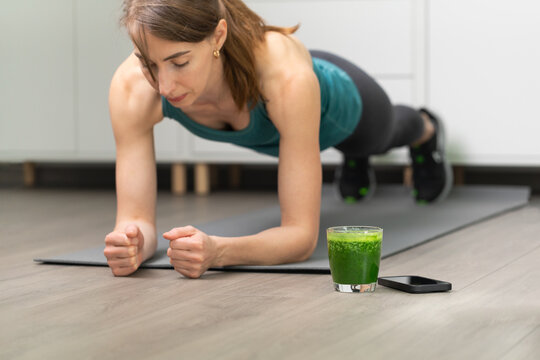 Women doing workout, planking on a gray mat. With smoothie for detox in background. Healthy living, dieting lifestyle.