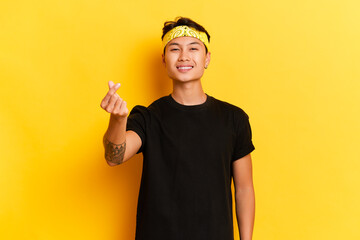 Young Asian guy wearing black T-shirt and yellow headband posing on yellow studio background copy...