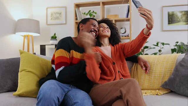 Selfie, home sofa and couple with happiness, love and funny hand gesture for mobile. Social media, profile picture and living room couch of young people sitting in the lounge feeling happy and silly