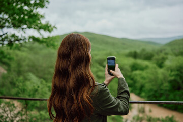 a woman in a raincoat takes pictures on the phone of a beautiful view of the forest. Travel, technology, mobile photography