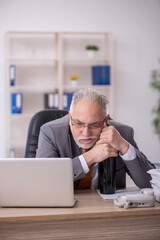 Old male employee drinking alcohol at workplace