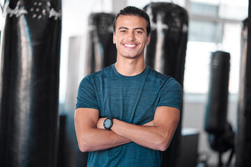 Fototapeta na wymiar Portrait, punching bag with a man boxer in the gym, standing arms crossed for fitness or motivation. Happy, exercise and confidence with a handsome young male training for boxing or a fight